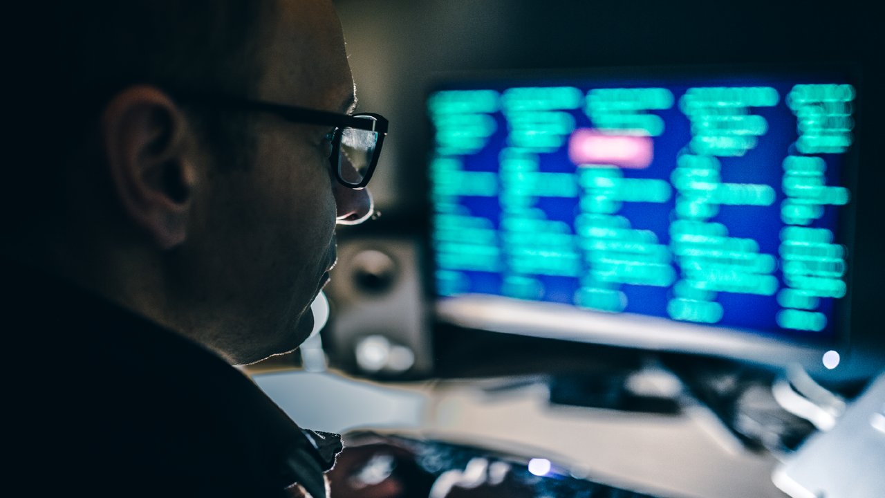 Data Compromise insurance coverage Computer hacker wearing glasses and using a computer in a dark room